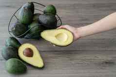 女人手持有减少一半切片新鲜的绿色鳄梨棕色（的）木表格水果健康的食物概念