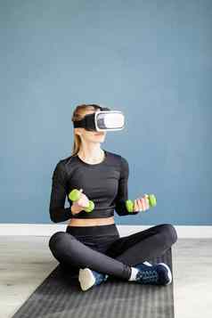 年轻的金发女郎女人体育运动衣服穿虚拟现实眼镜坐着健身席