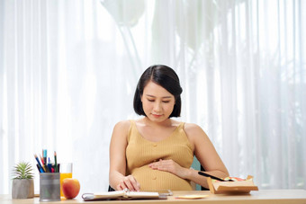 怀孕了年轻的女人坐着数字平板电脑表格生活房间早餐工作