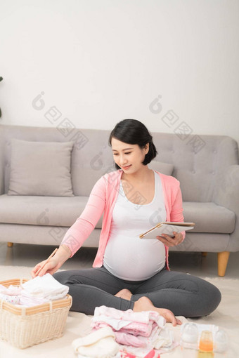 怀孕了女人首页地板上检查列表婴儿衣服准备孕妇医院
