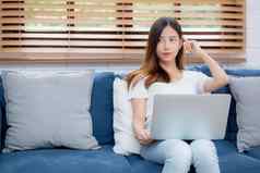 美丽的年轻的亚洲女人工作移动PC电脑思考的想法沙发首页自由女孩坐着沙发上笔记本互联网生活房间人生活方式概念