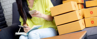 年轻的亚洲女人企业家电话写作订单客户在线笔记本首页在线购物物流交付女卖方工作沙发业务锻造