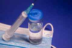 疫苗瓶小玻璃瓶标签蓝色的医疗面具医疗注射器注射针孤立的蓝色的背景治愈发展冠状病毒疫苗科维德