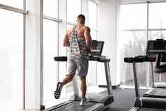 肌肉发达的运动健美运动员健身模型运行跑步机健身房大窗口