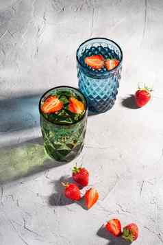 绿色蓝色的几何玻璃杯新鲜的水草莓水果色彩斑斓的影子光射线石头混凝土背景角视图