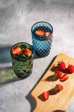 绿色蓝色的几何玻璃杯新鲜的水草莓水果色彩斑斓的影子光射线木切割董事会石头混凝土背景角视图