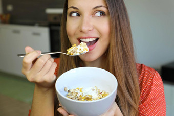 关闭美丽的年轻的女人吃斯凯尔酸奶麦片牛奶什锦早餐水果首页一边焦点模型眼睛室内图片健康的早餐概念