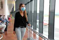 年轻的业务女人外科手术面具旅行电车行李走内部机场女执行手提箱业务旅行流感大流行