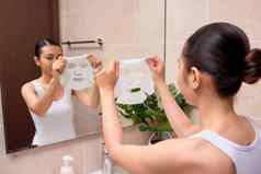 美丽的年轻的亚洲女人应用化妆品面部面具浴室