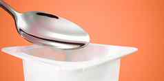 酸奶杯银勺子橙色背景白色塑料容器酸奶奶油新鲜的乳制品产品健康的饮食营养平衡