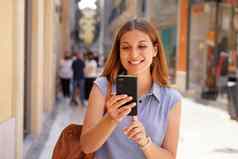肖像微笑年轻的女人走智能手机街