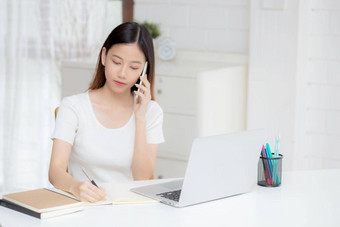 年轻的亚洲女人会说话的电话工作首页移动PC电脑自由女孩写作笔记本说话智能手机保持首页国内生活业务沟通概念