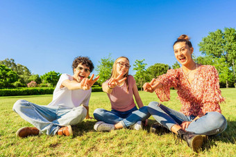 年轻的学生朋友坐着草城市公园显示胜利标志手指相机概念团结团结青年年龄快乐基因微笑自然