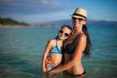 年轻的美丽的妈妈。可爱的女儿热带海滩