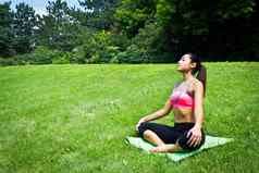 年轻的适合女人实践瑜伽公园冥想放松