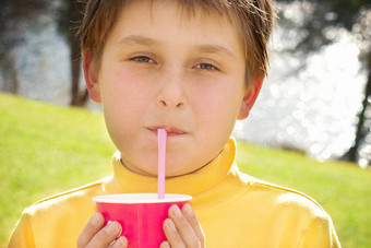 年轻的男孩喝草莓牛奶在户外