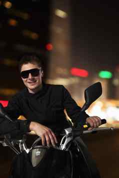 年轻的微笑男人。太阳镜坐着摩托车晚上北京