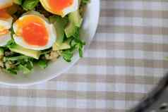 沙拉鳄梨藜麦芝麻菜半熟的鸡蛋白色板特写镜头前视图健康的健康的健康的早餐概念