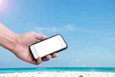手持有智能手机海滩蓝色的天空背景
