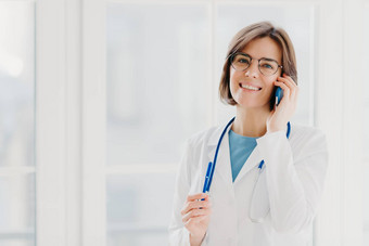 积极的女人医生咨询病人手机gladfully相机持有笔穿白色外套提出了医疗办公室提出了窗口医疗保健咨询概念