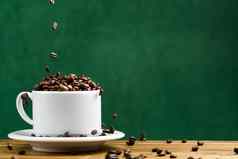 国际一天咖啡概念特写镜头白色咖啡杯完整的咖啡豆子咖啡豆子秋天白色杯子分配黑暗绿色背景