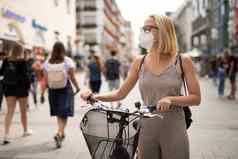 女人走自行车行人城市街穿医疗脸面具公共防止传播电晕病毒正常的科维德疫情