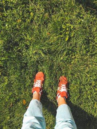 女人红色的运动鞋站草草坪上前视图脚明亮的体育运动鞋子光蓝色的牛仔裤户外休闲活动休闲装自然夏天背景