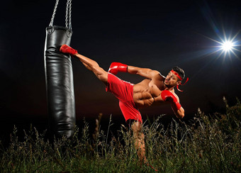 运动员培训黑色的晚上背景拳击手红色的短裤红色的拳击手套肌肉肌肉发达的身体晚上培训培训开放空间一边踢冲袋黑色的冲袋