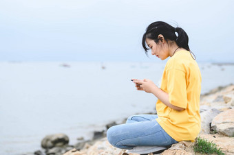 年轻的亚洲女<strong>人</strong>智能手机海边脸面具删除呼吸新鲜的空气疫苗接种科维德冠状病毒<strong>疫情人</strong>生活方式健康概念