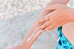 手年轻的女孩涂片防晒霜太阳保护手背景海滩特写镜头