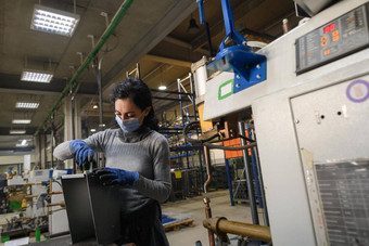 女人工作金属行业生产机器穿脸面具工作由于冠状病毒流感大流行