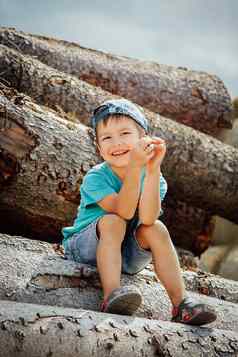 男孩蓝色的棒球帽牛仔布短裤坐在日志笑着说愉快地