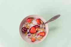 碗牛奶什锦早餐酸奶新鲜的樱桃草莓饮食早餐碗燕麦片浆果新鲜的牛奶绿色背景健康饮食概念