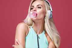 美丽的金发女郎女人吹粉红色的泡沫口香糖女孩听音乐耳机时尚生活方式肖像