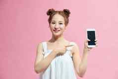 肖像微笑休闲女孩指出手指空白屏幕移动电话孤立的粉红色的背景