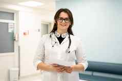 自信微笑年轻的女人医生站医疗机构骄傲专业医生治疗师女人眼镜相机医院走廊肖像一般医生
