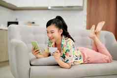 年轻的微笑亚洲女人智能手机购买在线购物信贷卡说谎沙发首页