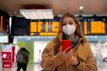 旅行者女人穿断续器脸面具火车站女通勤检查智能手机时间表离职移民
