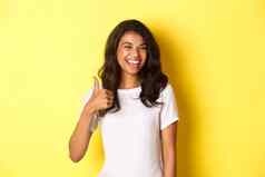 肖像快乐满意非裔美国人女学生显示竖起大拇指眨眼微笑很高兴批准好赞扬站黄色的背景