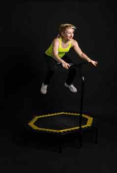 女孩健身蹦床黑色的背景黄色的t恤黑色的健身房女人活动运动员生活方式有氧运动重量反弹迷你有氧运动年轻的肌肉教练享受