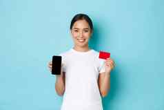 电子商务购物生活方式概念快乐的亚洲女孩白色t恤显示信贷卡智能手机屏幕推荐应用程序在线购买交易