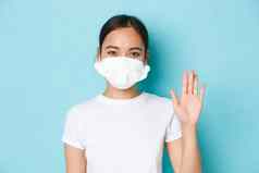 科维德社会距离冠状病毒流感大流行概念友好的微笑亚洲女孩呼吸器问候人挥舞着手光蓝色的背景