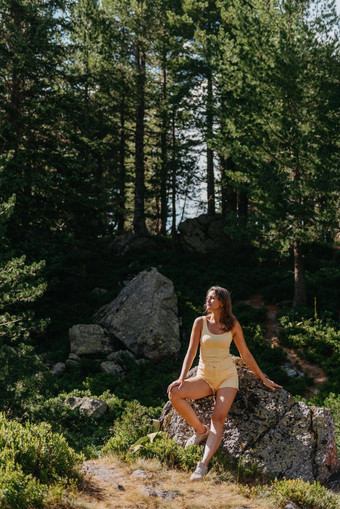 漂亮的年轻的女孩黄色的t恤黄色的短裤坐着石头美丽的峡谷旅行者山赶时髦的人女孩山时尚的女人网纹衬衫坐着石头森林旅游热概念徒步旅行旅行夏天神秘的木美丽的自然