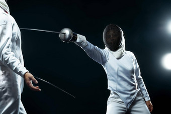 击剑运动员专业体育竞技场年轻的击剑运动员穿面具白色击剑服装持有剑黑色的背景灯