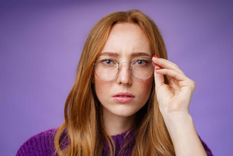 不确定严肃的表情集中红色头发的人女人皱着眉头眯着眼看规定眼镜相机触碰框架阅读标志解决谜题紫色的背景