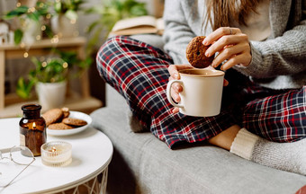 舒适的女人腿针织冬天温暖的袜子毛衣网纹睡衣喝热可可咖啡杯子坐着沙发上首页秋天情绪蜡烛装饰饼干室内植物