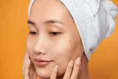 脸亚洲女人微笑触碰脸穿毛巾护肤品美容概念橙色背景