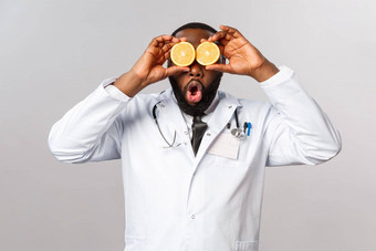 医疗保健健康的饮食疾病概念有趣的好看的医生非裔美国人医生玩橙色逗乐保持安全吃维生素水果灰色背景