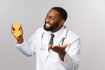 医疗保健健康的饮食疾病概念英俊的厚颜无耻的非裔美国人医生指出病人解释方法住安全吃维生素持有橙子微笑