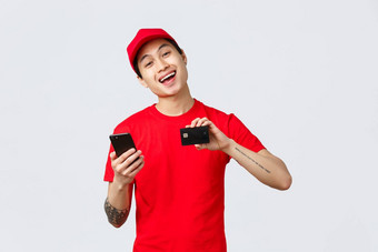 友好的交付的家伙红色的统一的t恤帽显示智能手机屏幕信贷卡推荐应用程序跟踪订单在线购物快递做广告航空公司服务